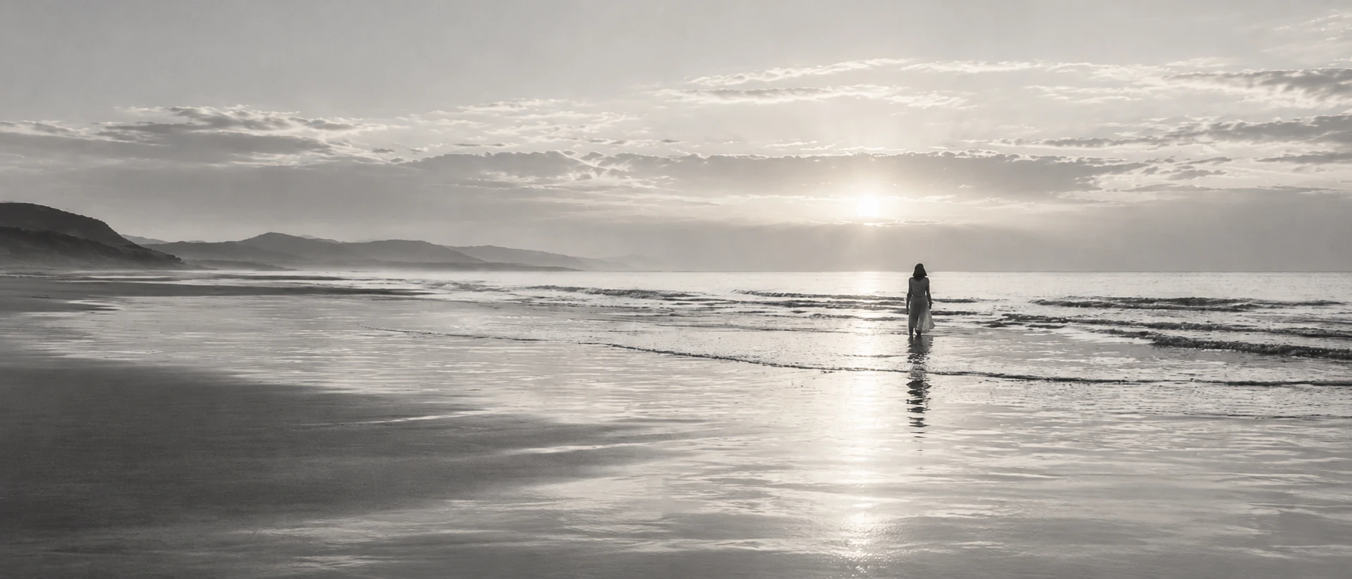 A lone figure at a bright, distant shoreline in black and white.